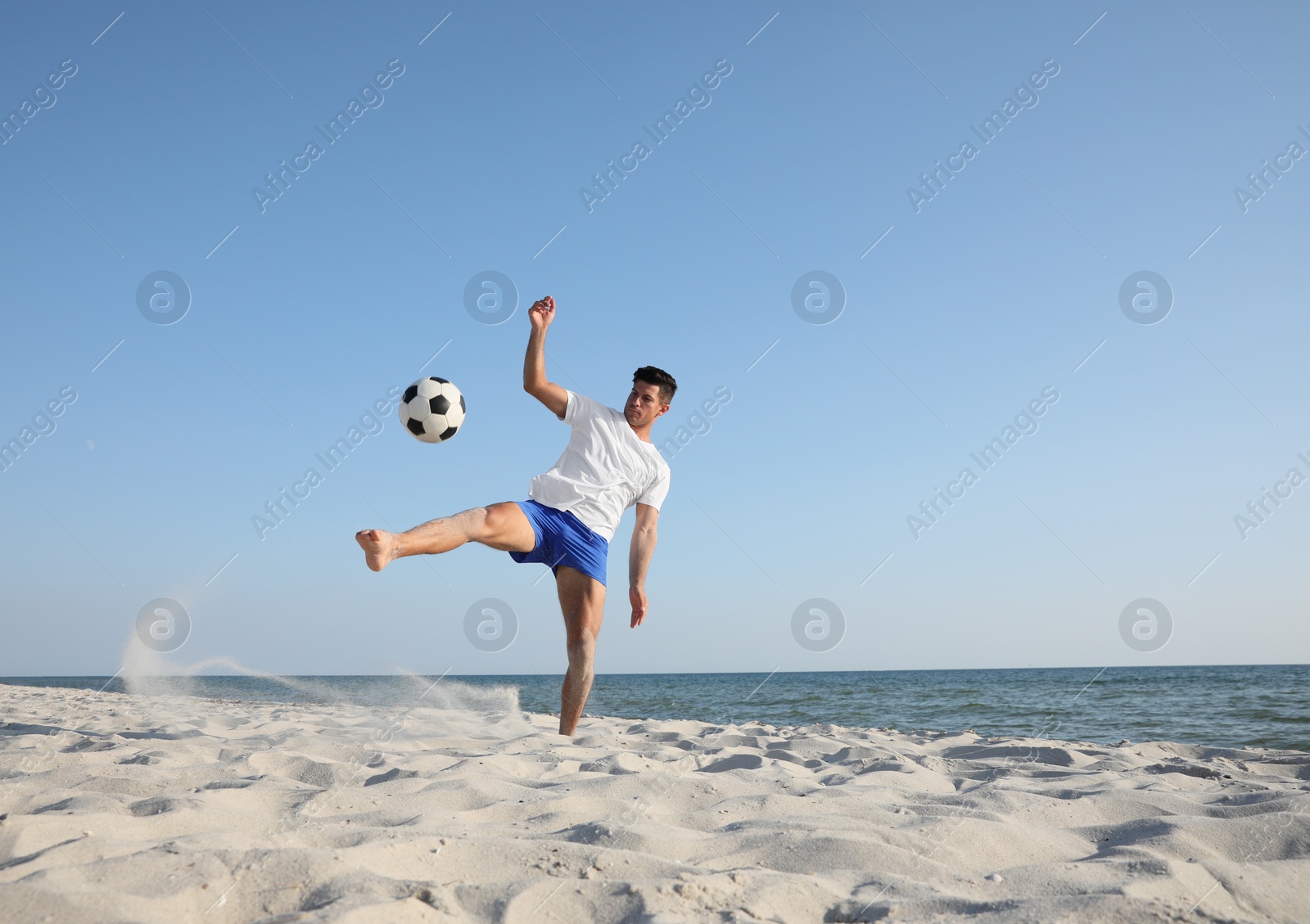 Photo of Man kicking football ball on beach near sea