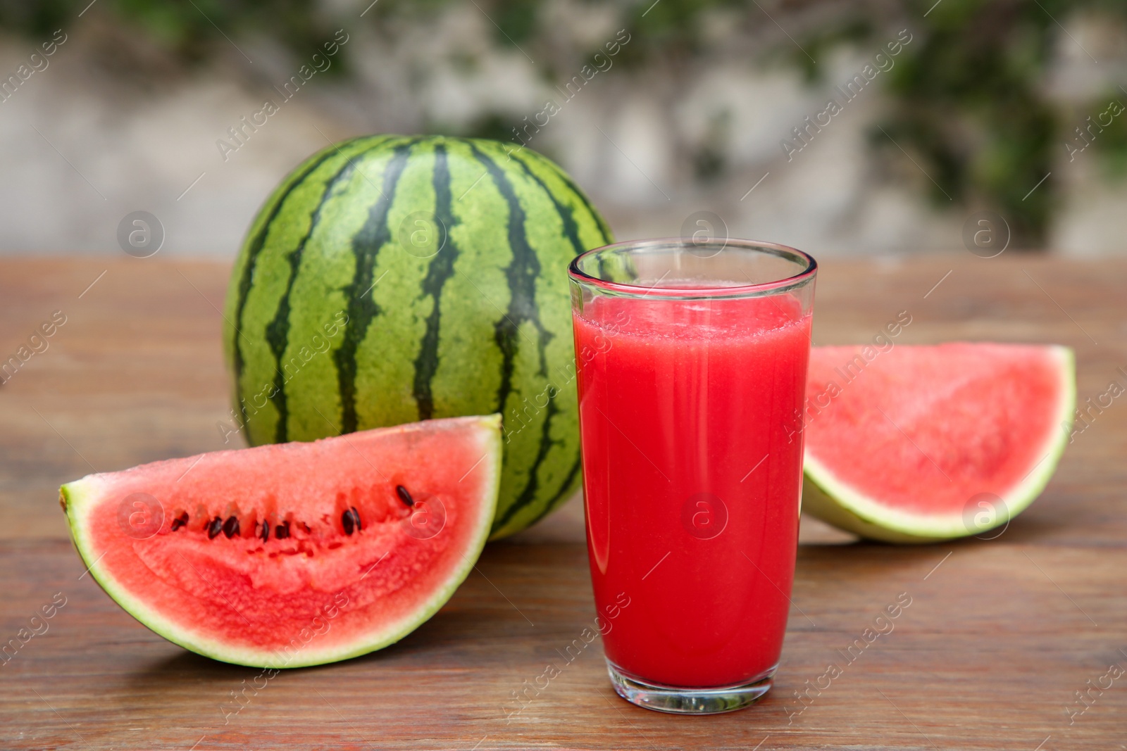 Photo of Delicious ripe watermelons and glass of fresh juice on wooden table outdoors