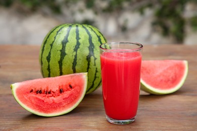 Delicious ripe watermelons and glass of fresh juice on wooden table outdoors