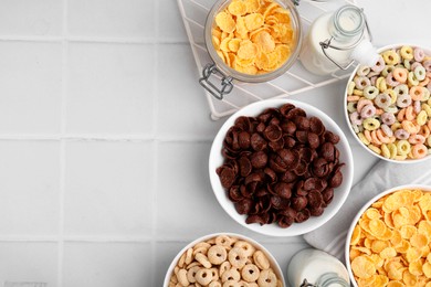 Photo of Different delicious breakfast cereals and milk on white tiled table, flat lay. Space for text