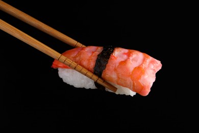 Chopsticks with delicious nigiri sushi on black background, closeup