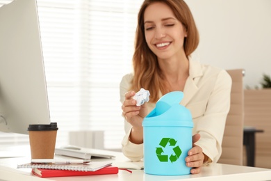 Young woman throwing paper into mini recycling bin at office