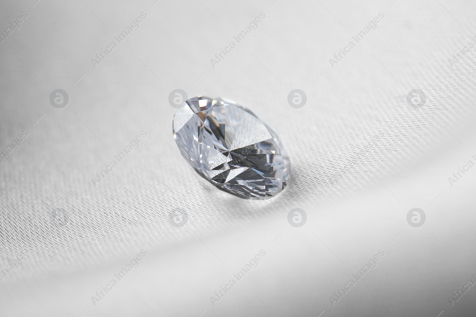 Photo of Beautiful shiny diamond on white fabric, closeup