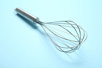 Photo of Metal whisk on light blue background, closeup