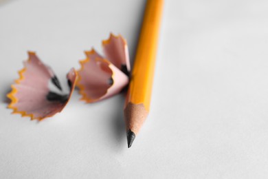 One sharp graphite pencil and shavings on white background, closeup