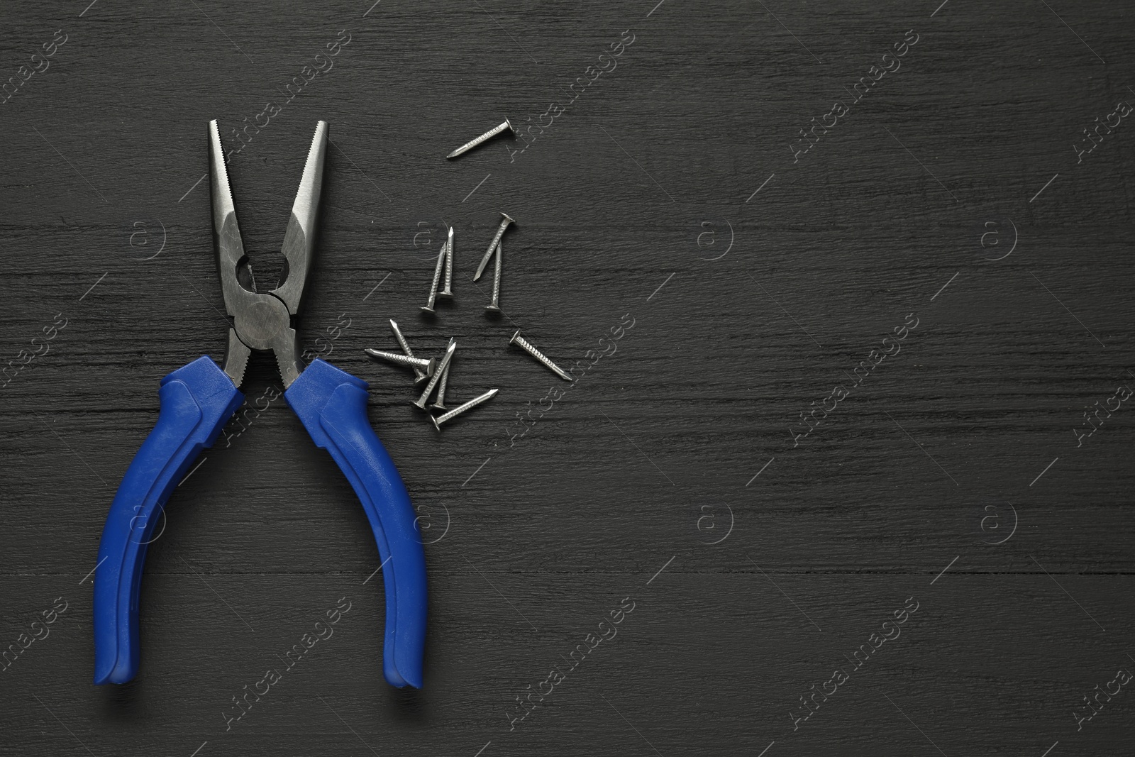 Photo of Needle nose pliers and nails on black wooden table, flat lay. Space for text