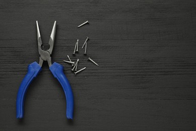 Photo of Needle nose pliers and nails on black wooden table, flat lay. Space for text