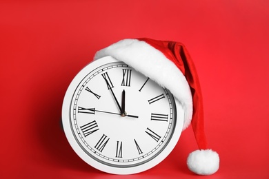 Photo of Clock with Santa hat showing five minutes until midnight on red background. New Year countdown