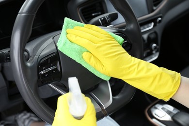 Photo of Woman cleaning steering wheel with rag in car, closeup