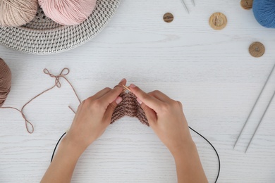 Photo of Top view of young woman knitting with needles at white wooden table, closeup. Engaging in hobby