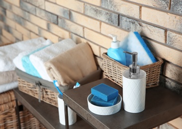 Dish with soap bars and bottle of shampoo on table near brick wall