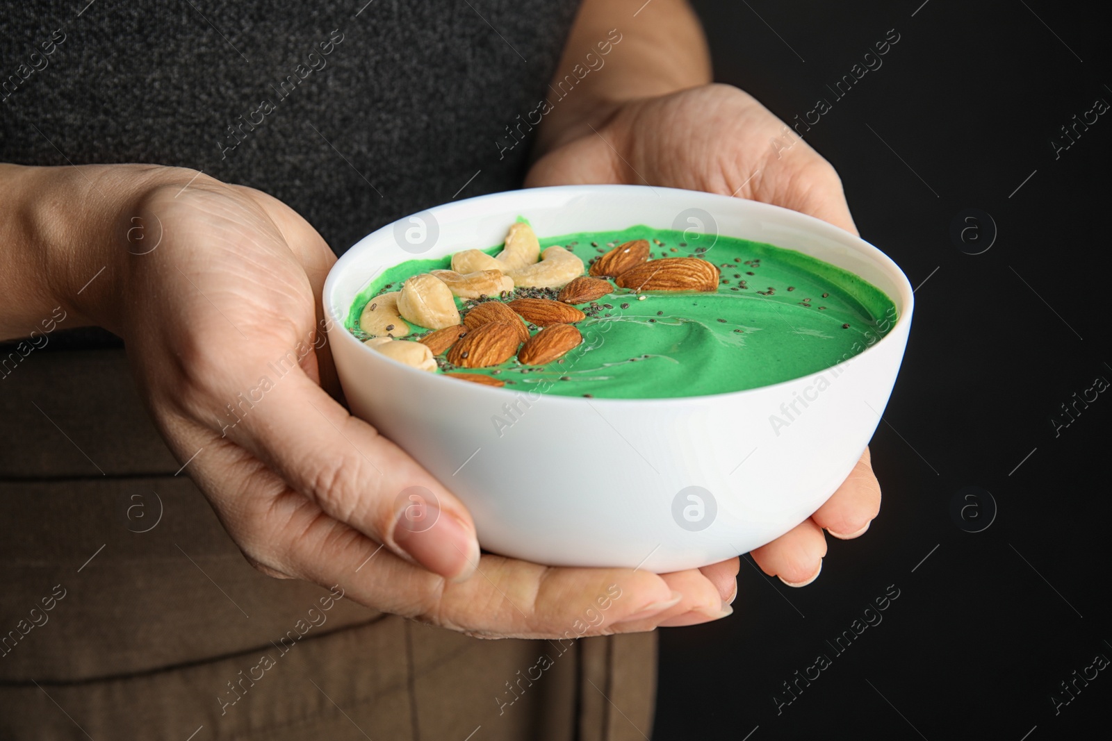 Photo of Woman holding bowl of spirulina smoothie with nuts and chia seeds, closeup