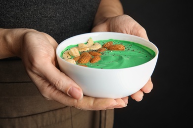 Photo of Woman holding bowl of spirulina smoothie with nuts and chia seeds, closeup