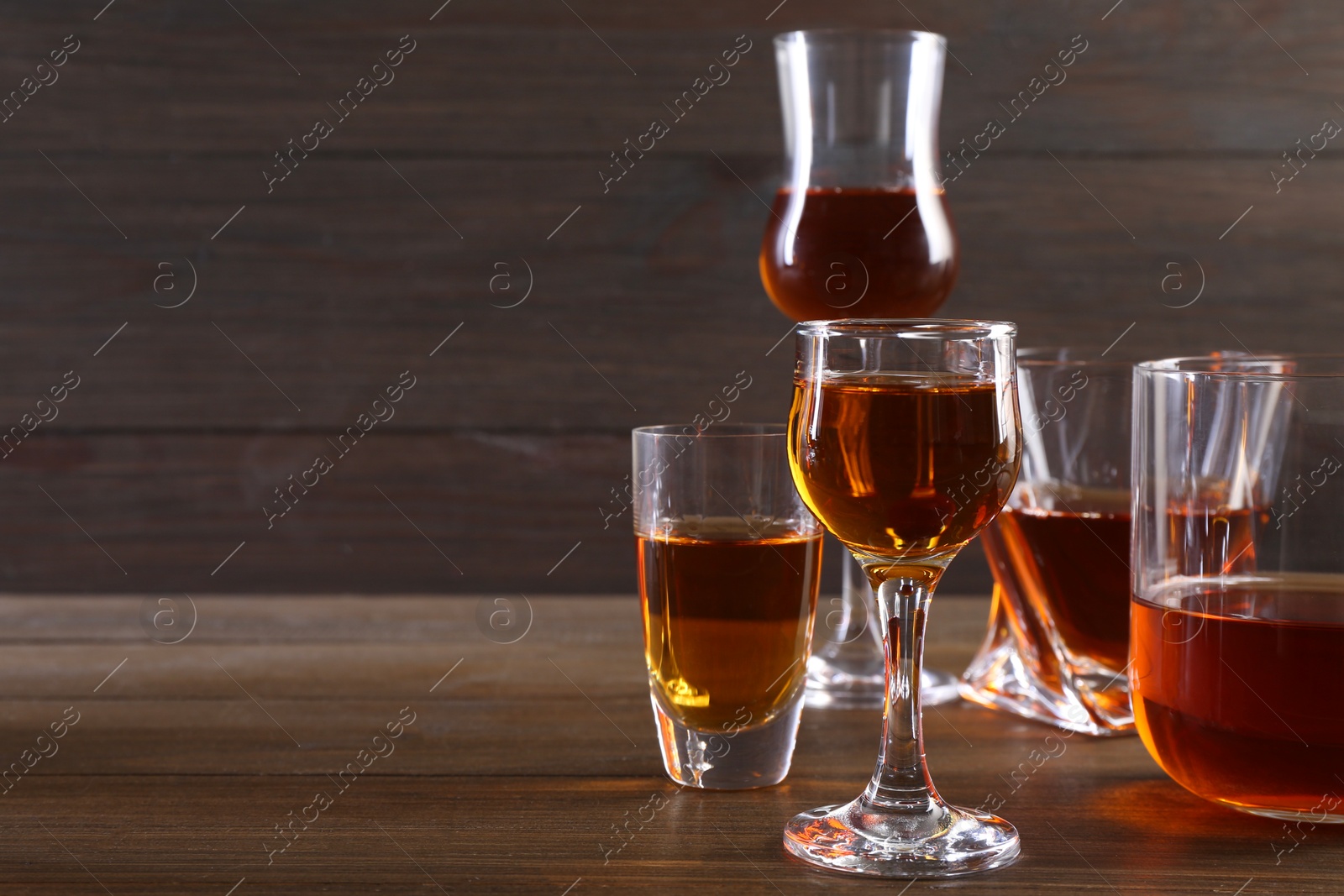 Photo of Different delicious liqueurs in glasses on wooden table, space for text