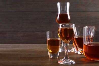 Photo of Different delicious liqueurs in glasses on wooden table, space for text