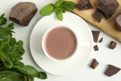 Photo of Cup of delicious hot chocolate, chunks and fresh mint on white wooden table, flat lay