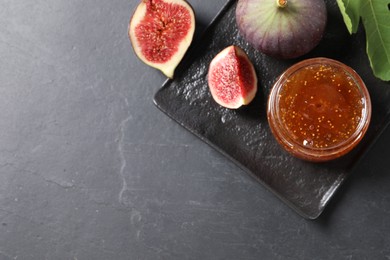Photo of Jar of tasty fig jam and fresh fruits on black table, flat lay. Space for text