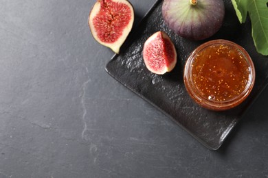 Jar of tasty fig jam and fresh fruits on black table, flat lay. Space for text