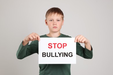 Photo of Boy holding sign with phrase Stop Bullying on light grey background