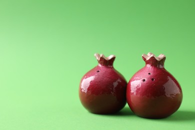 Photo of Pomegranate shaped salt and pepper shakers on green background. Space for text