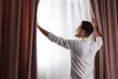 Happy man opening window curtains at home