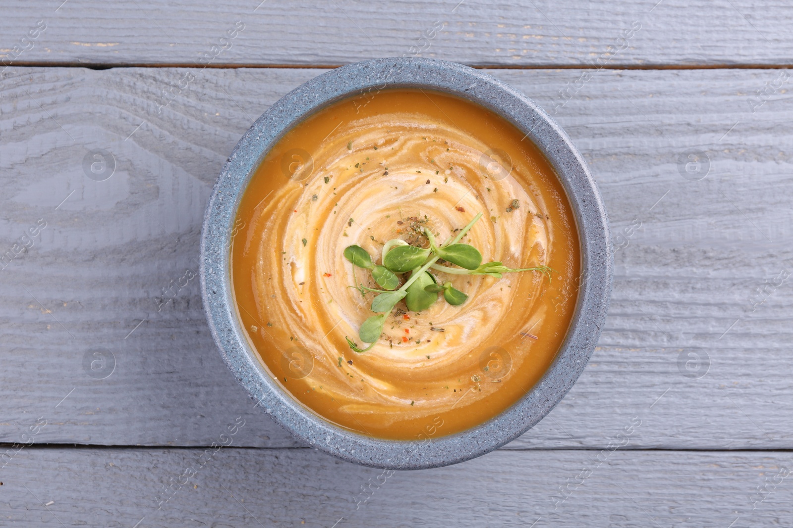 Photo of Bowl of delicious pumpkin soup with microgreens on grey wooden table, top view