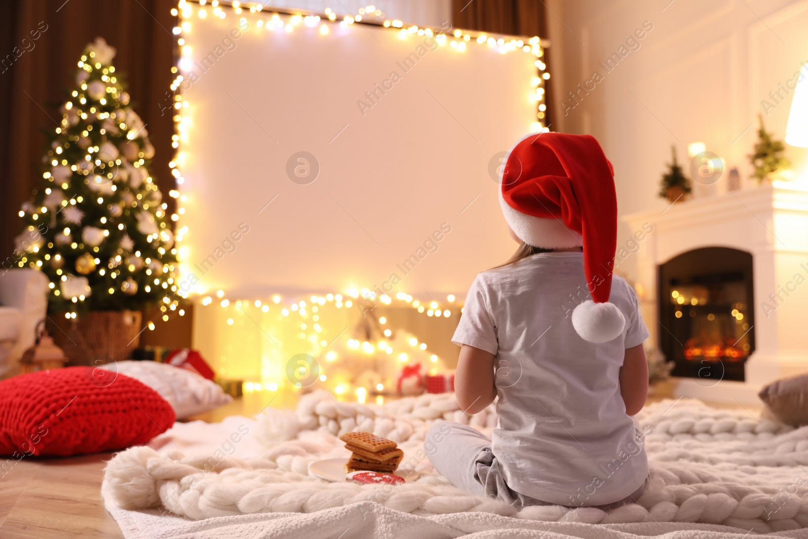 Photo of Little girl watching movie using video projector at home. Cozy Christmas atmosphere