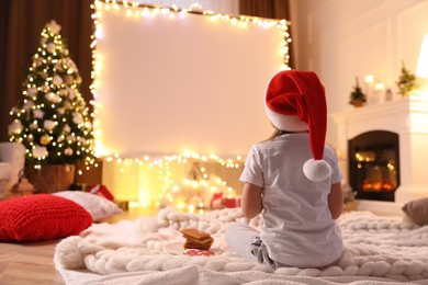 Photo of Little girl watching movie using video projector at home. Cozy Christmas atmosphere