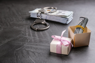 Photo of Dollar bills, gift box and handcuffs on grey stone table, space for text. Bribe concept