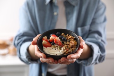 Photo of Woman holding bowl of tasty granola with berries, yogurt and seeds indoors, closeup