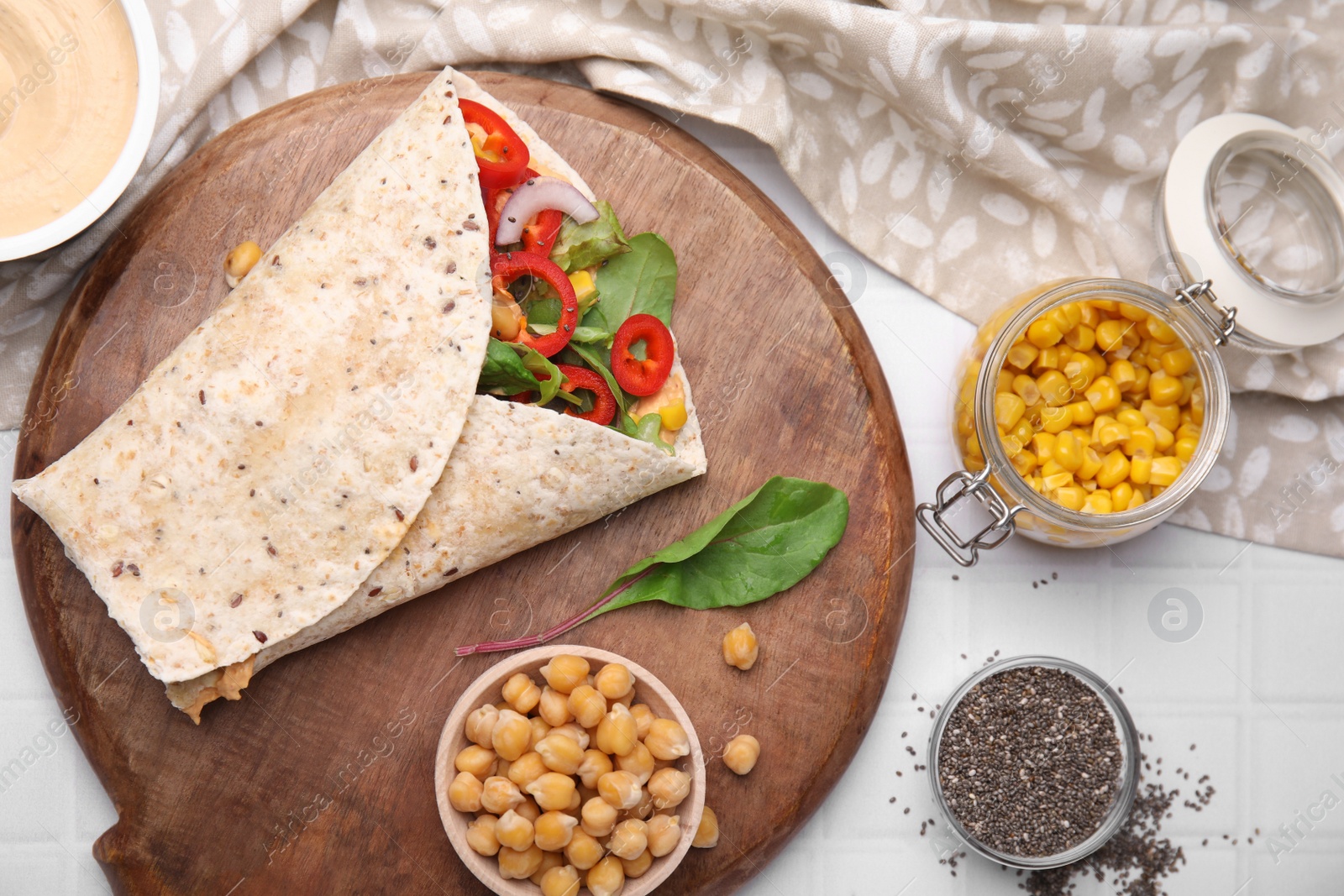 Photo of Board with delicious hummus wrap and vegetables on white table, flat lay