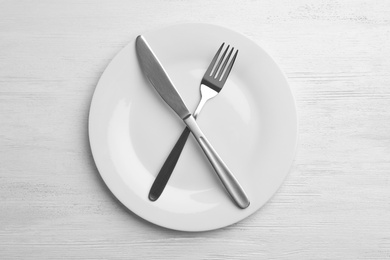 Photo of Empty plate with cutlery on white wooden background, flat lay