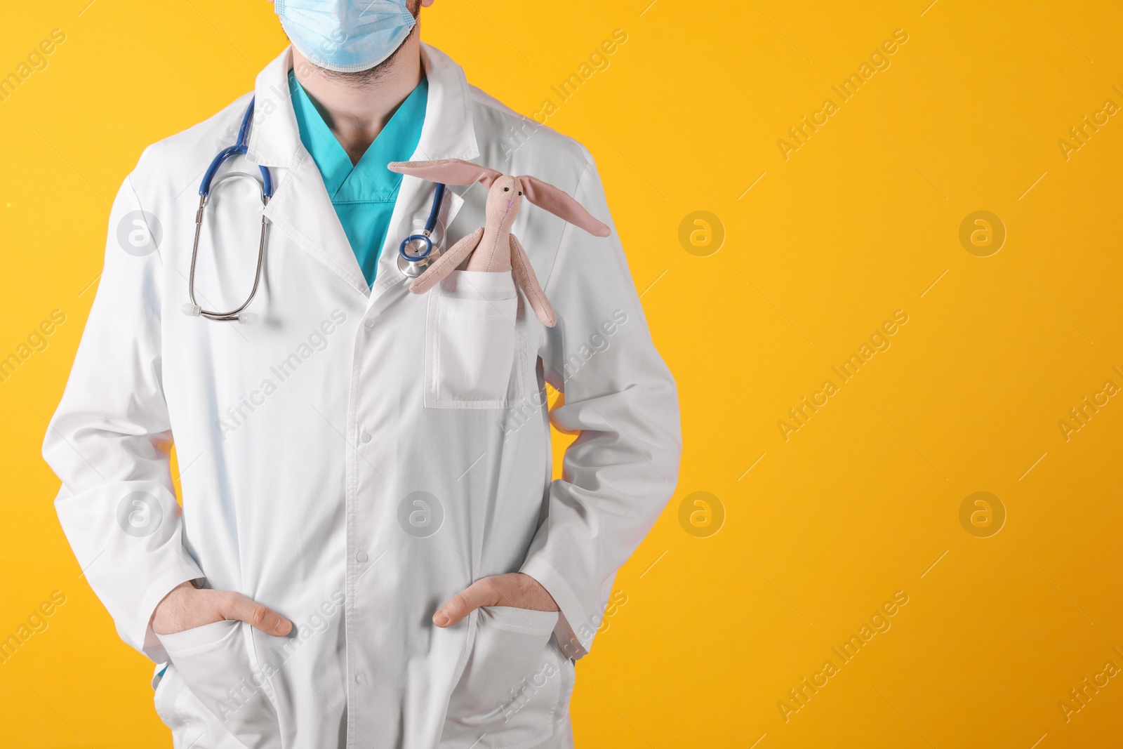 Photo of Pediatrician with toy bunny and stethoscope on yellow background, closeup. Space for text