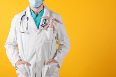 Pediatrician with toy bunny and stethoscope on yellow background, closeup. Space for text