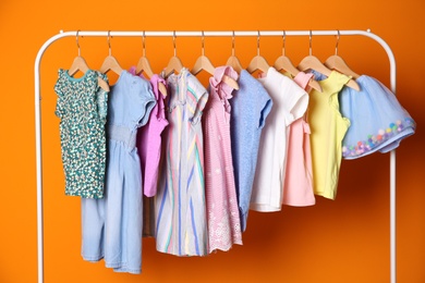 Rack with stylish child clothes on color background