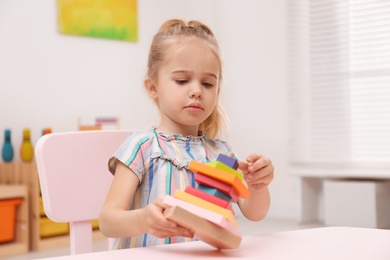 Cute child playing with colorful wooden stacker at table in room