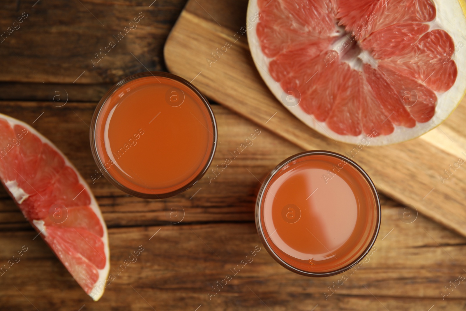 Photo of Glasses of pink pomelo juice and fruit on wooden table, flat lay