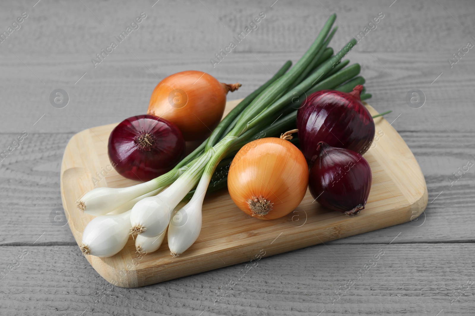 Photo of Board with different kinds of onions on grey wooden table, closeup