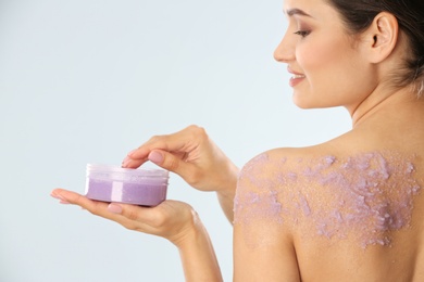 Young woman applying natural scrub on her body against light background