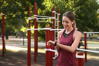 Young woman with wireless headphones and smart watch listening to music on sports ground