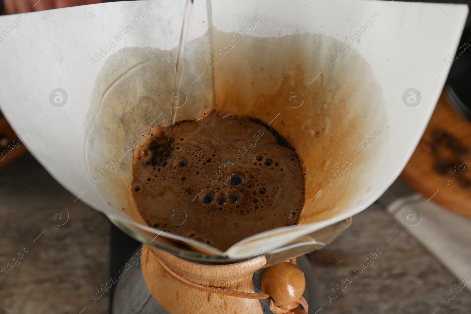 Photo of Pouring hot water into glass chemex coffeemaker with paper filter at table, closeup