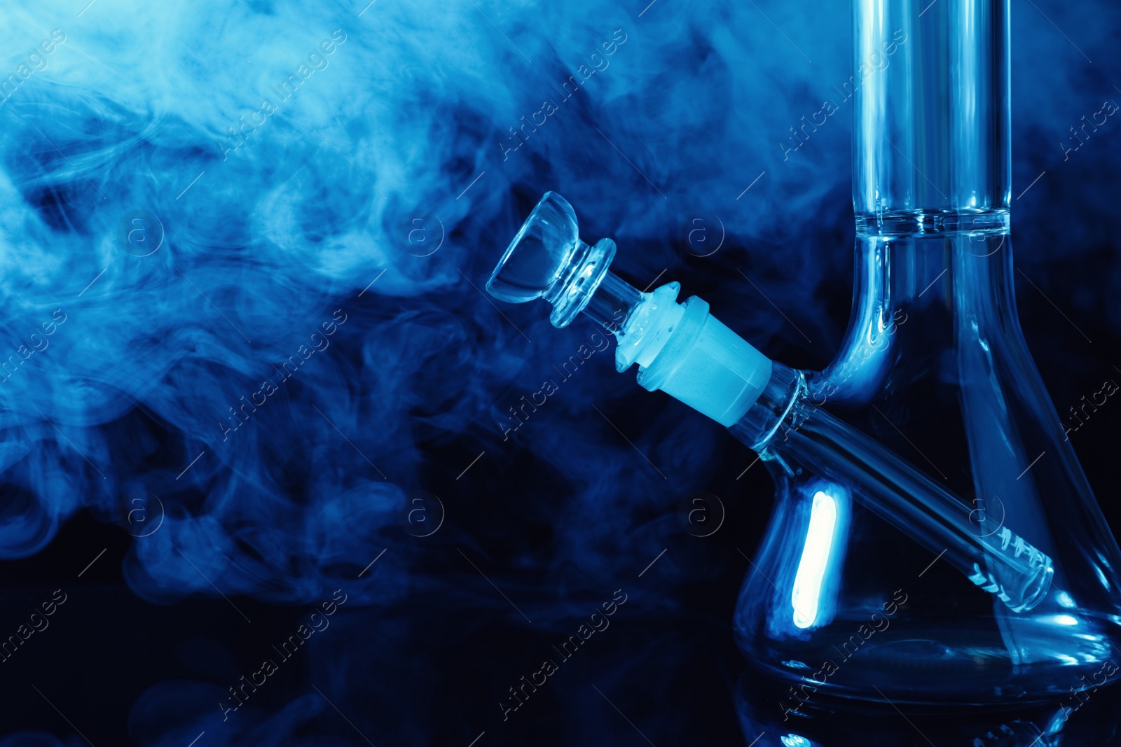 Photo of Closeup view of glass bong with smoke on black background, space for text. Smoking device