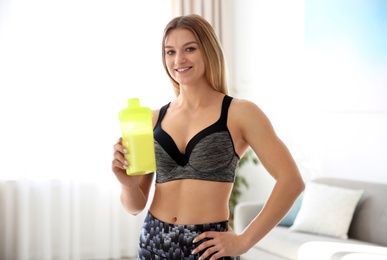 Photo of Young sporty woman with bottle of protein shake at home
