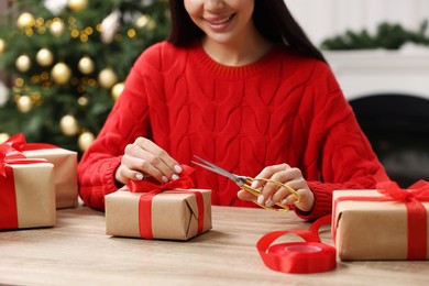 Photo of Woman decorating Christmas gift box at wooden table indoors, closeup