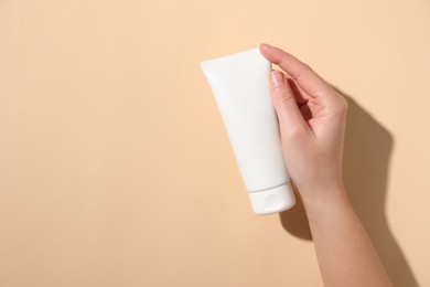 Photo of Woman with tube of hand cream on beige background, top view. Space for text