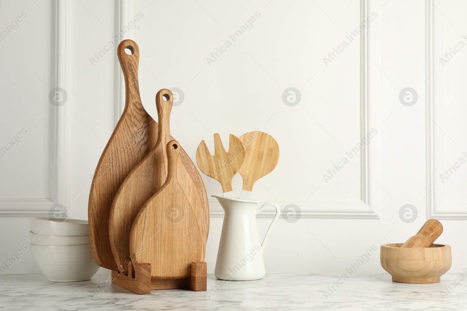 Photo of Wooden cutting boards, kitchen utensils and dishware on white marble table