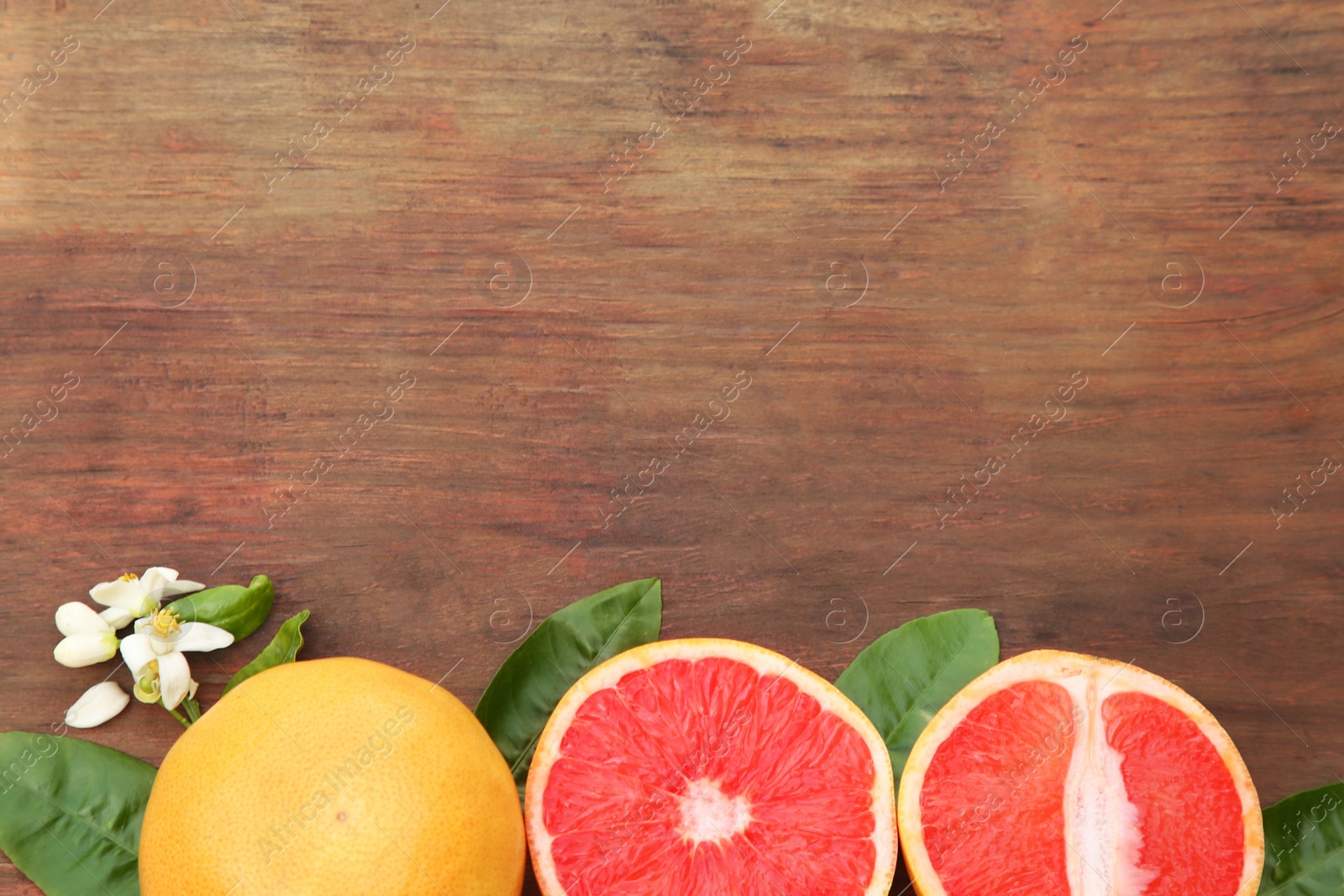 Photo of Fresh ripe grapefruits and green leaves on wooden table, flat lay. Space for text