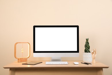 Photo of Comfortable workplace with blank computer display on desk and plant near beige wall. Space for text