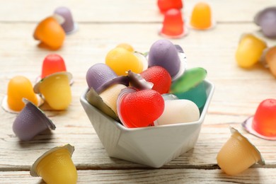 Photo of Bowl with tasty bright jelly cups on white wooden table