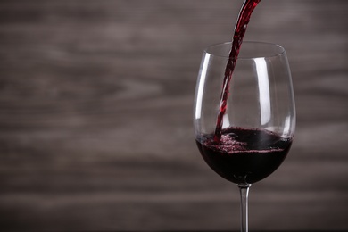 Photo of Pouring wine into glass on wooden background, space for text